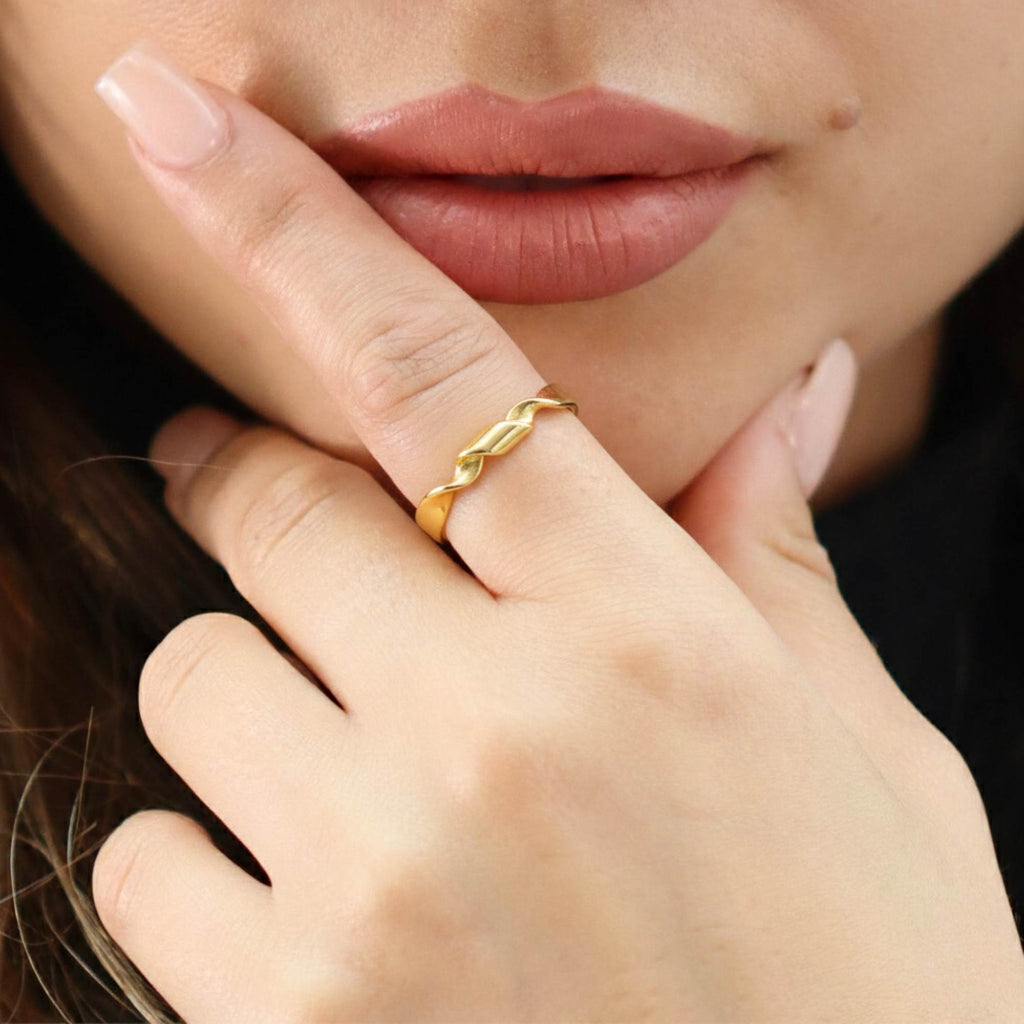 Close-up of a hand wearing a gold open adjustable ring by Satinski with a blurred background
