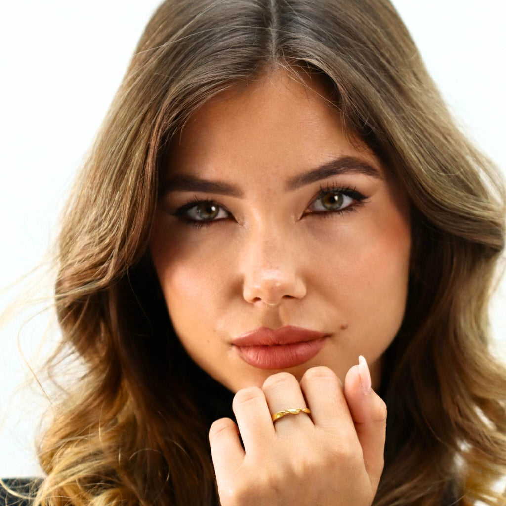 Close-up of a woman with wavy hair and a gold ring on her finger against a white background